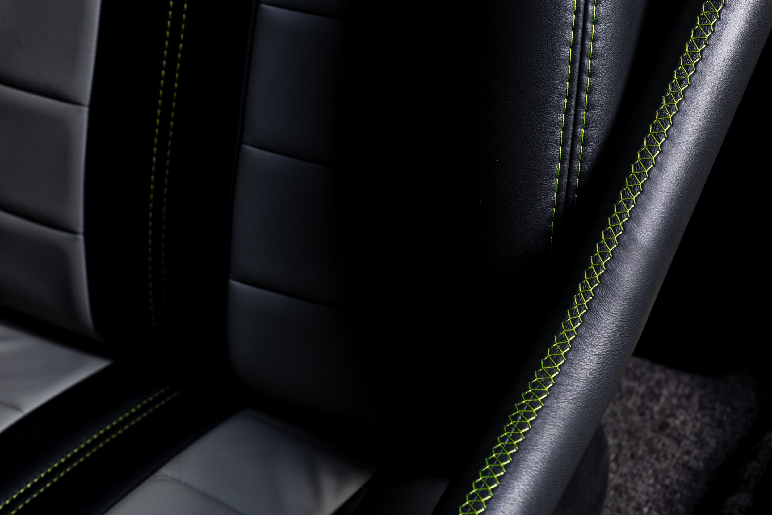 Close-up of black leather car seat with bright green stitching details.