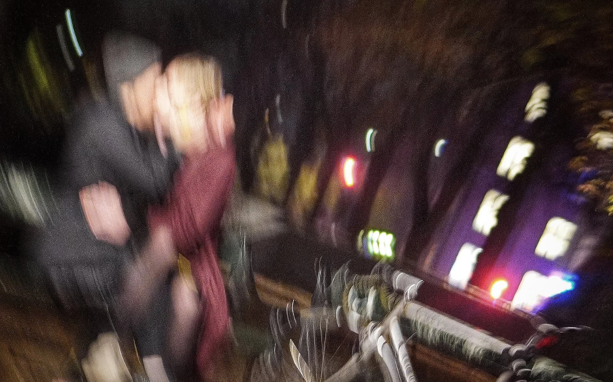 Billedet er uskarpt og viser to personer, en mand og en kvinde, der går på en bygade om aftenen. Der er lyse neonskilte og bygninger i baggrunden.