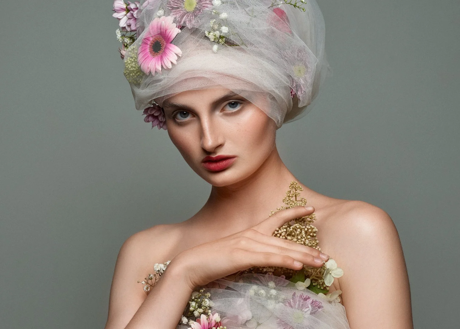 Æstetisk portræt af kvinde med tyl og blomster i håret, minimalistisk baggrund og intens blik