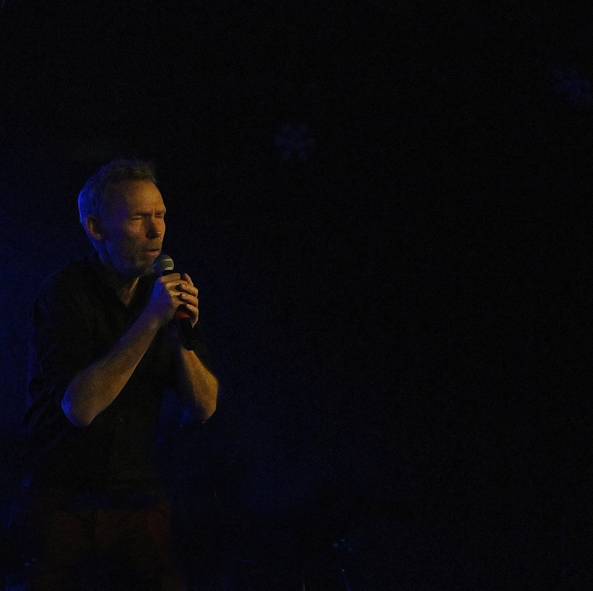 Intens liveoptræden med sanger i spotlight
Mørk scene med mandlig sanger i koncentreret optræden under blå scenelys