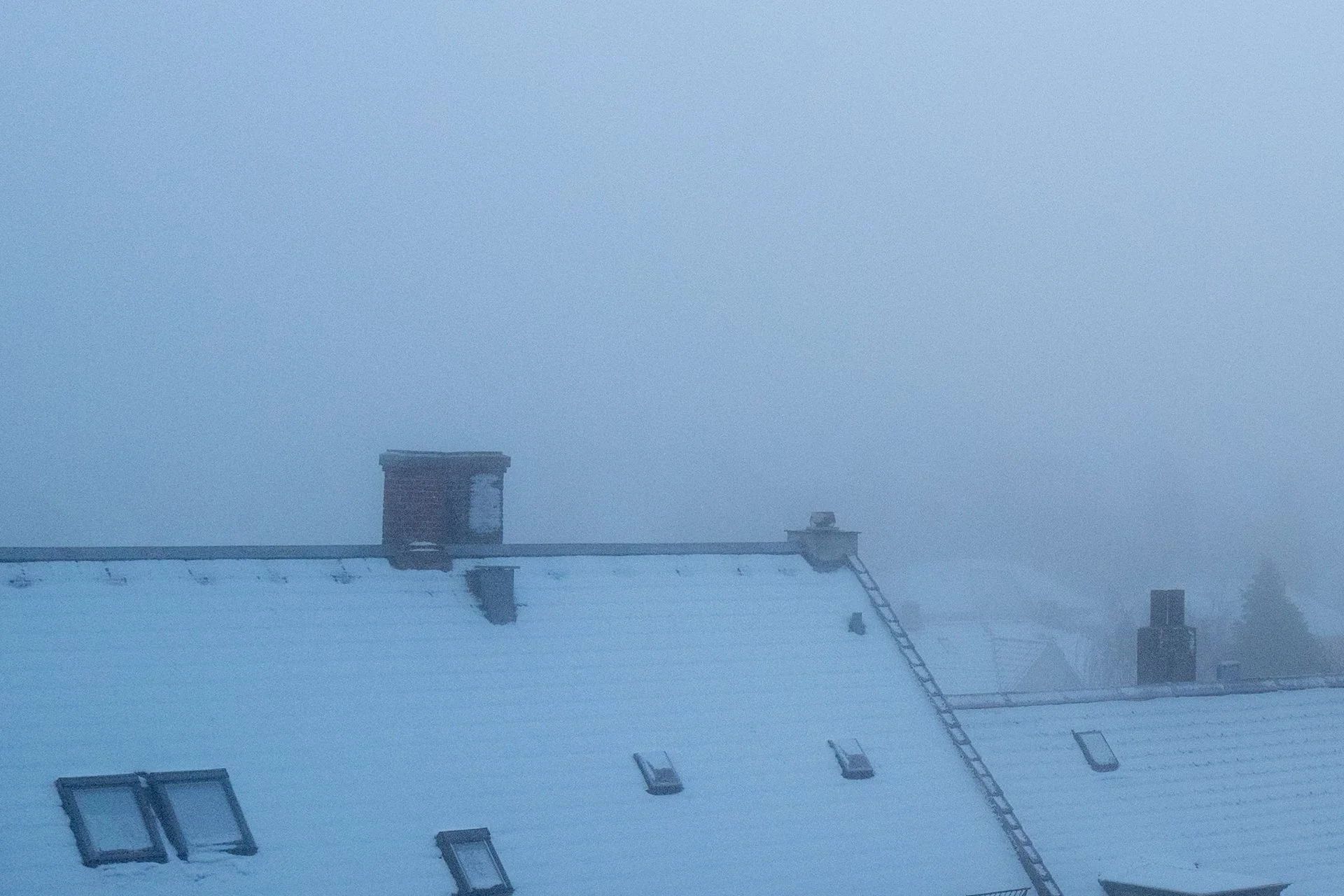 Snedækket tag og skorsten i tæt tåge en vintermorgen. Et stemningsfuldt vinterbillede med sneklædte tage og tyk tåge. Perfekt til blogs om vinter, arkitektur eller nordisk minimalisme.