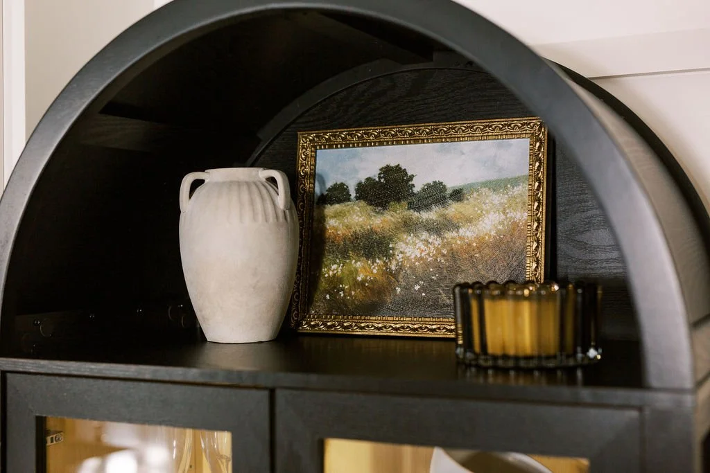 Decorative shelf with a white vase, a framed landscape painting, and a small container.