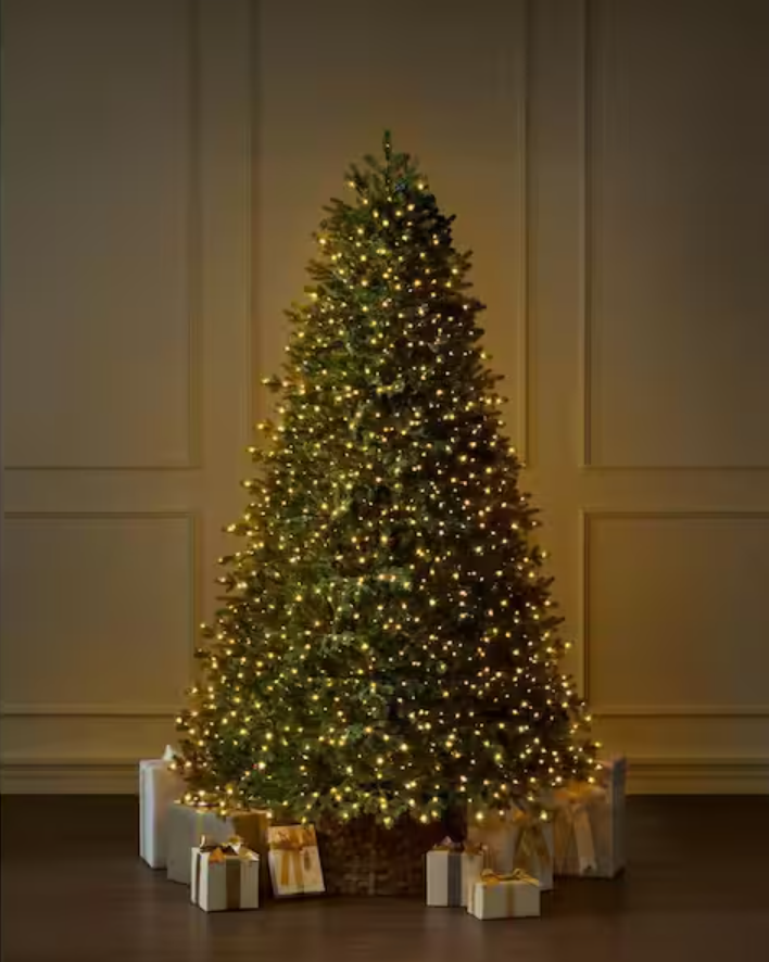 Decorated Christmas tree with yellow lights and wrapped presents underneath in a room with cream-colored paneled walls.