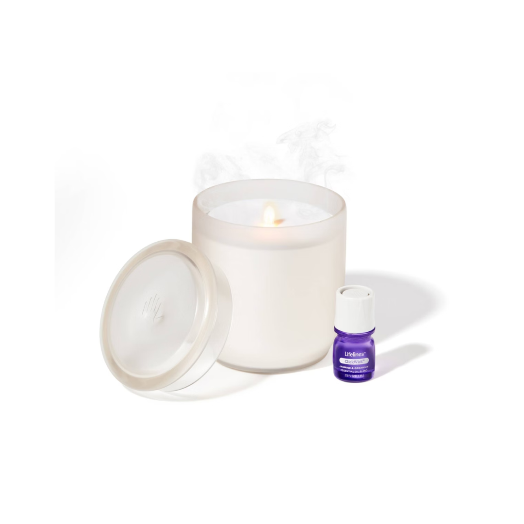 A white candle burning inside a glass jar with a lid, a small purple essential oil bottle, and a purple and white aromatherapy diffuser.