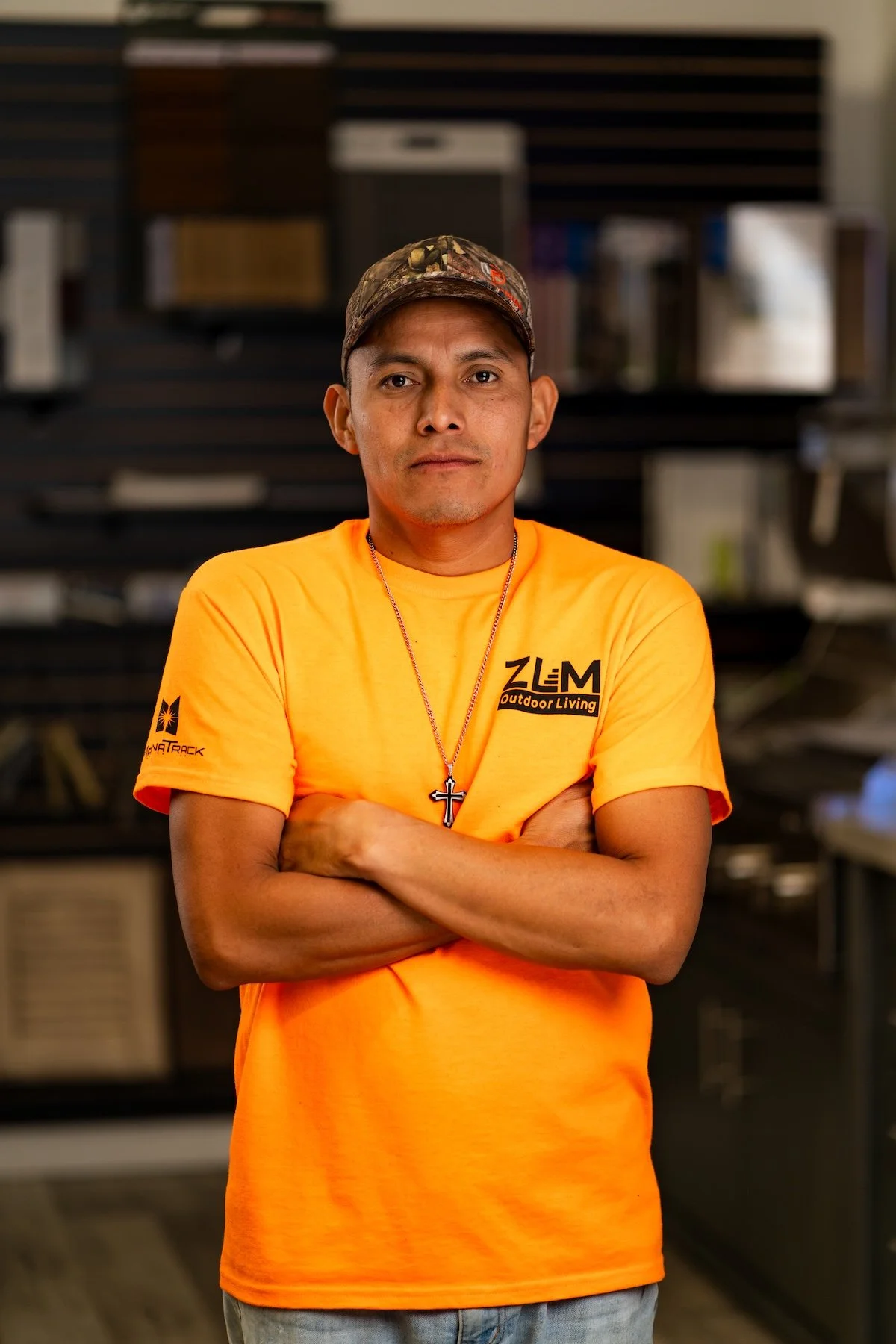 Man wearing a black hoodie with orange logo standing in a warehouse with wood samples in the background.