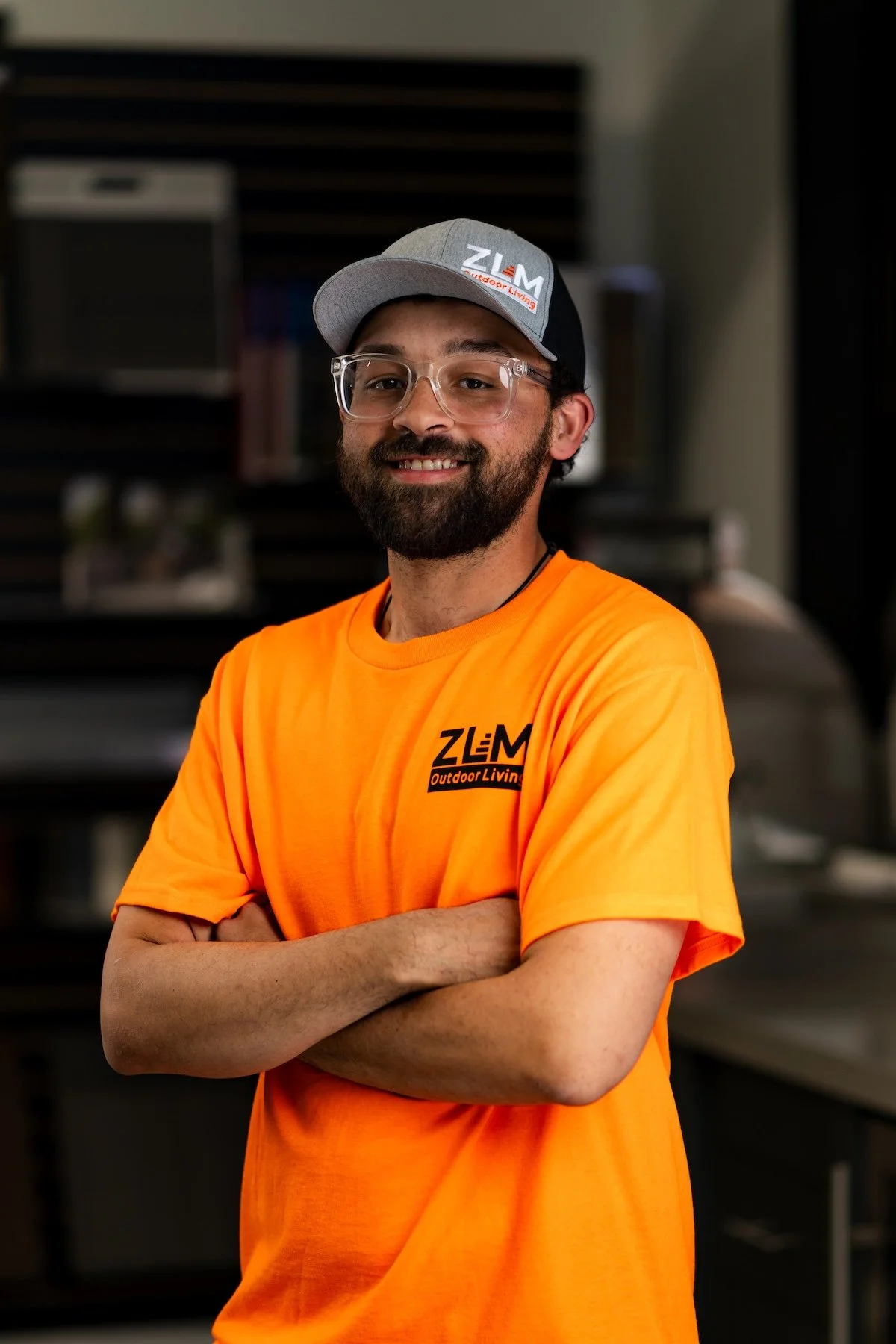 Man wearing glasses with clear frames and orange t-shirt with ZLM logo