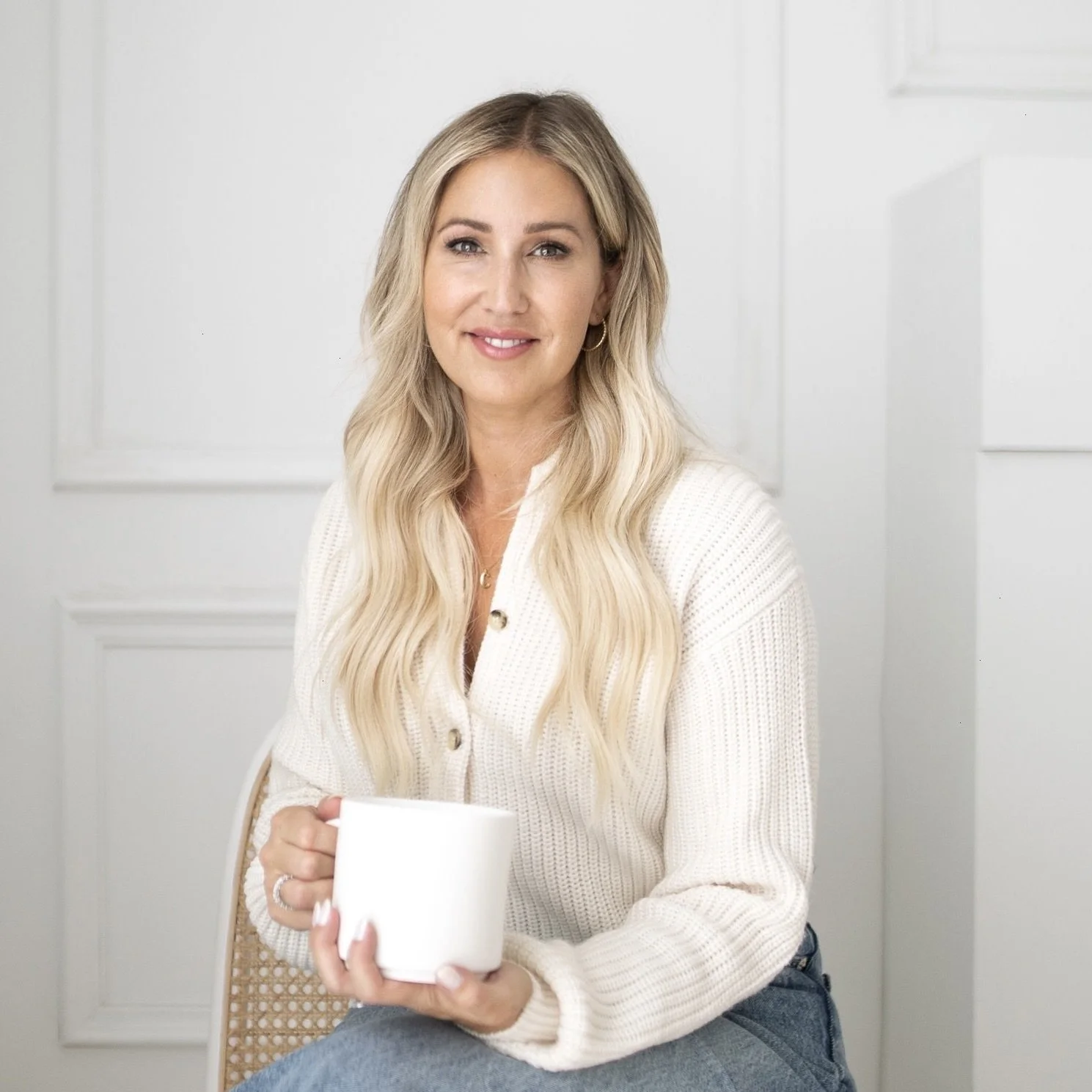 carina sitting on a chair holding a coffee mug facing forward with a smile