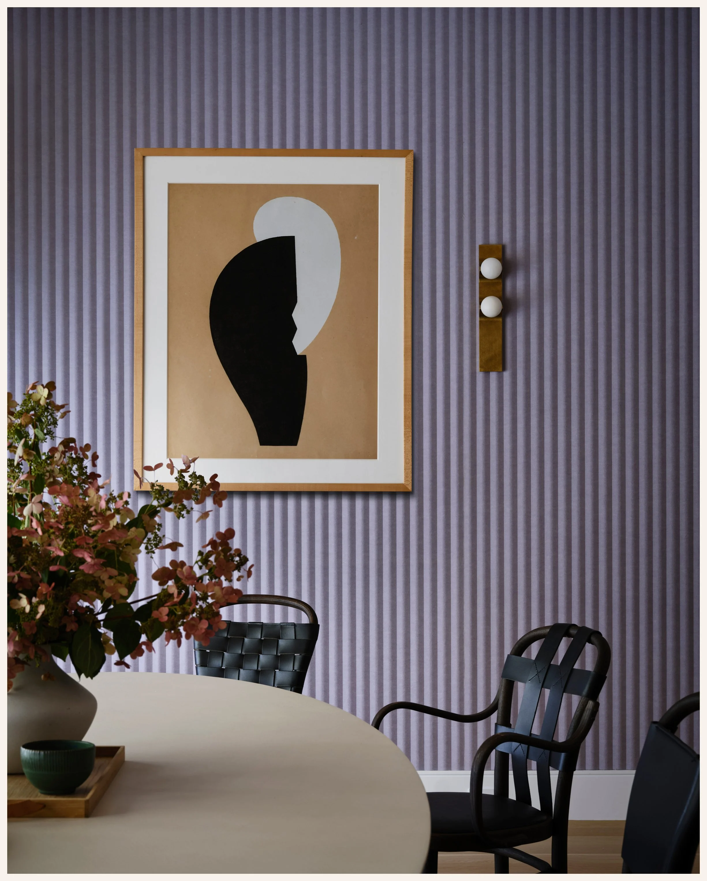 A dining room with a purple striped wall, a modern abstract artwork, and a table with black chairs and a floral centerpiece.
