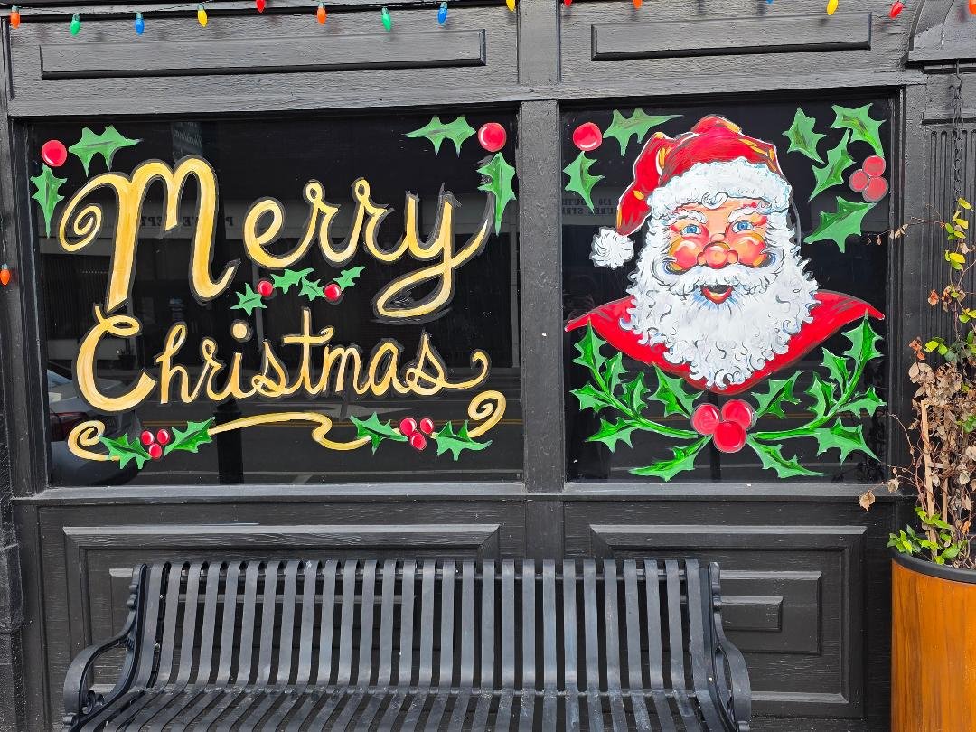 dr.canvas hand painted Holiday window display with a Santa face and a message wishing Merry Christmas.