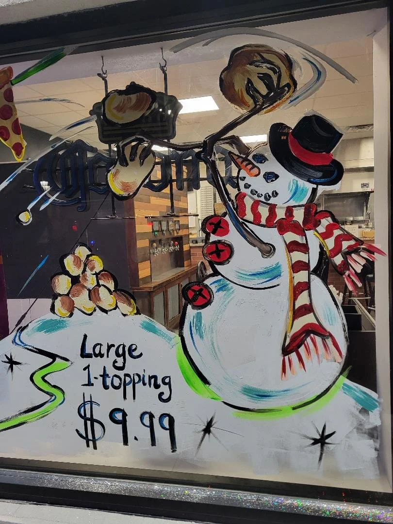 Colorful hand-painted sign advertising a large ice cream sundae with one topping for $9.99, featuring a snowman wearing a top hat, scarf, and buttons, holding a spoon, with scoops of ice cream on its head, decorated with sprinkles and mock cherries.