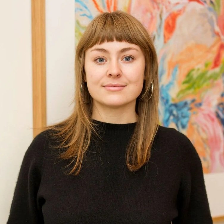A woman with shoulder-length light brown hair, blue eyes, and a black turtleneck smiling at the camera.
