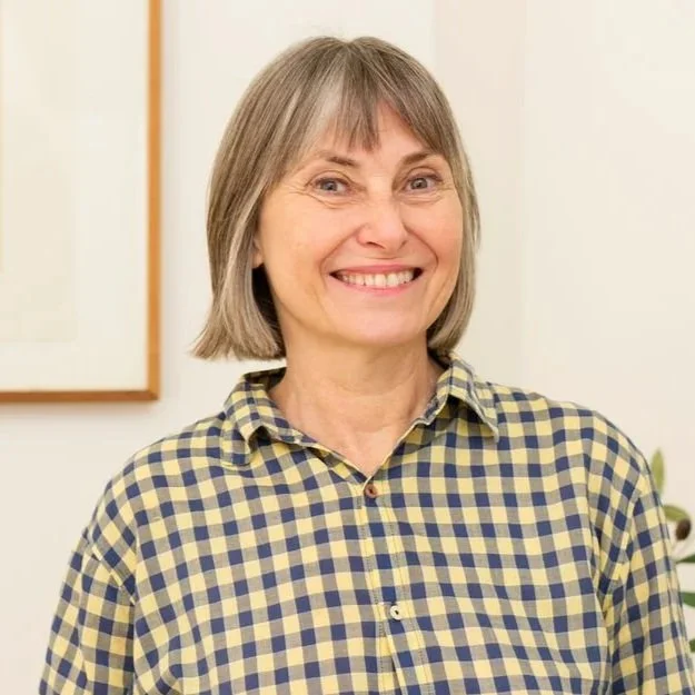 A smiling middle-aged woman with short gray hair wearing a brown sweater.