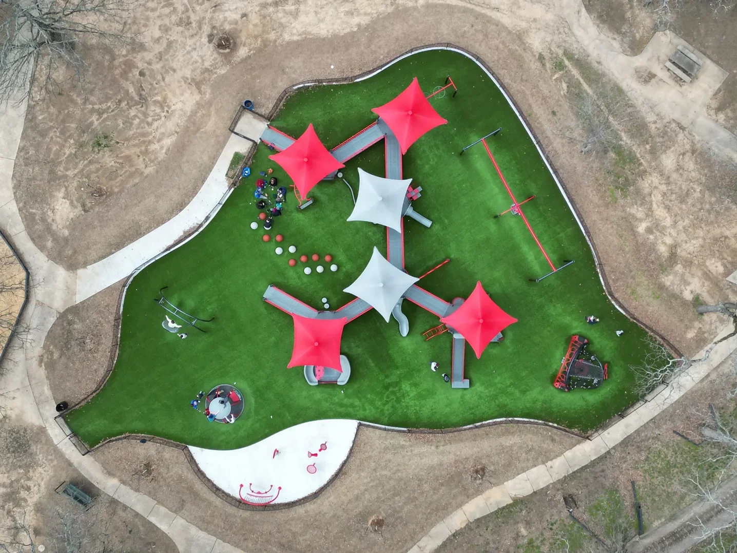 Aerial view of a green playground with colorful shade canopies, climbing structures, slides, and play equipment.