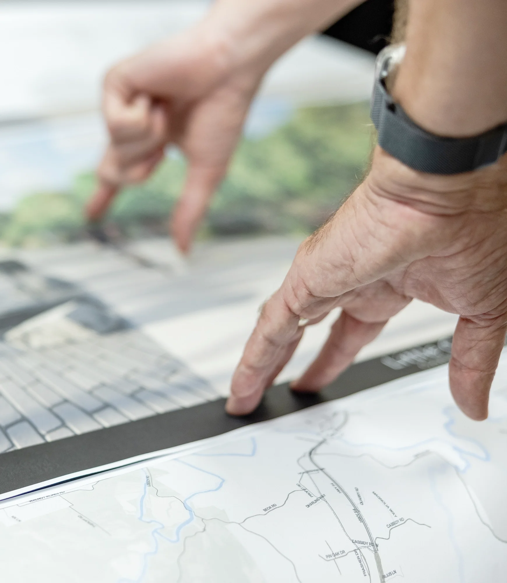 Close-up of a person using a touchscreen map and laptop while planning a route.