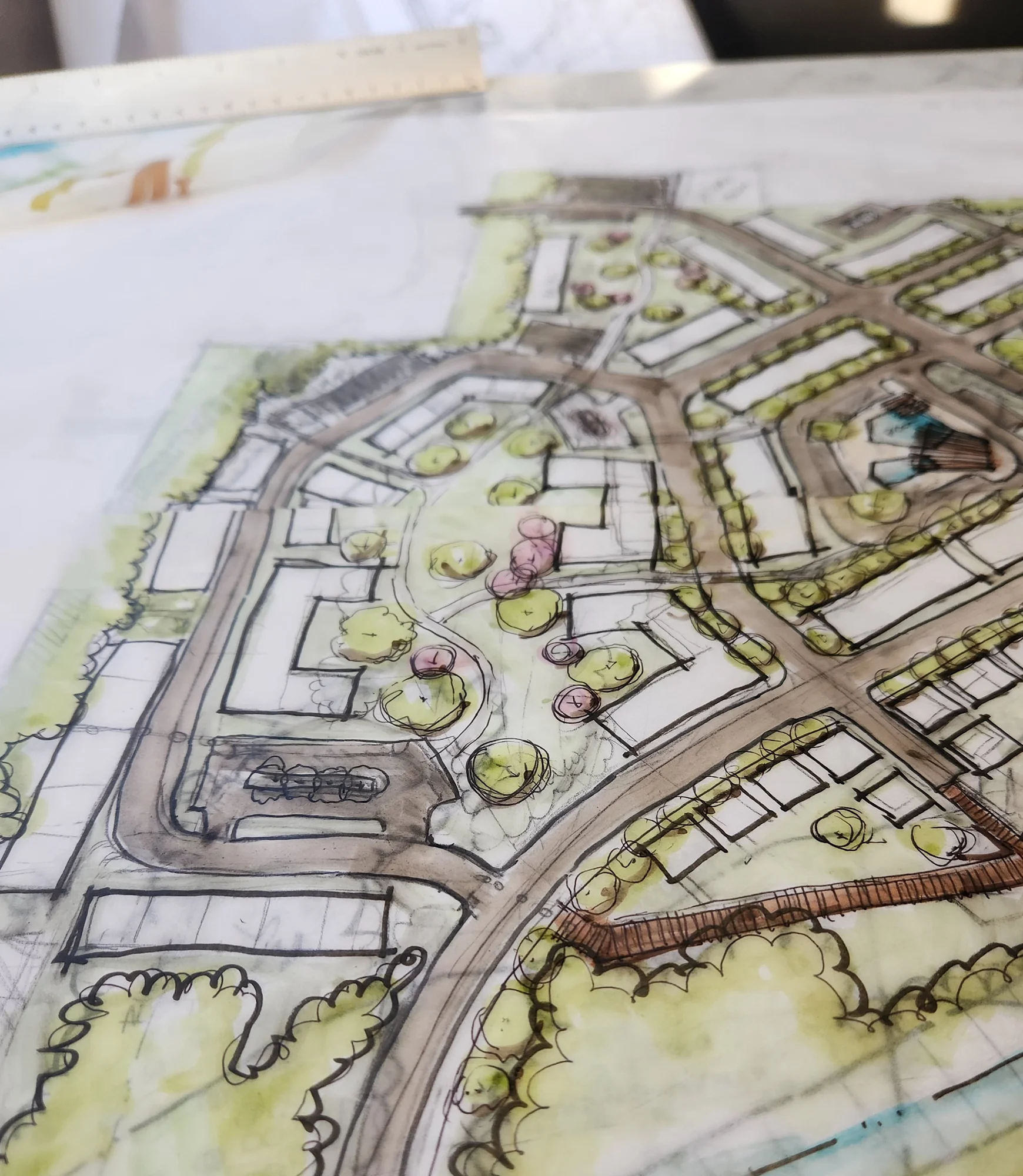 Hand-drawn architectural site plan showing roads, buildings, landscaped courtyards, trees, and a pedestrian bridge