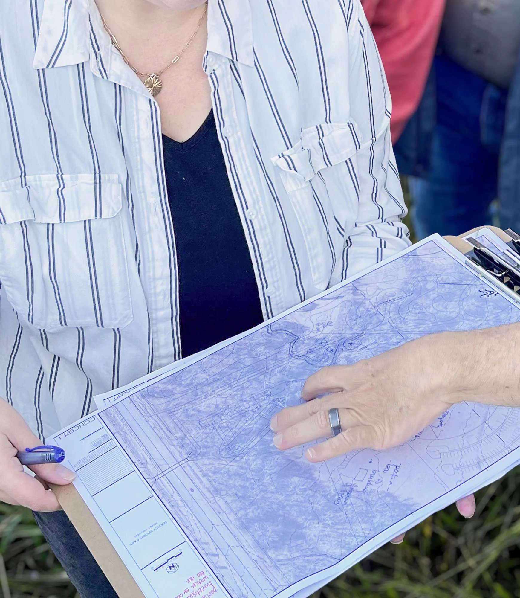 Person in a white striped shirt reviewing architectural blueprints on a clipboard