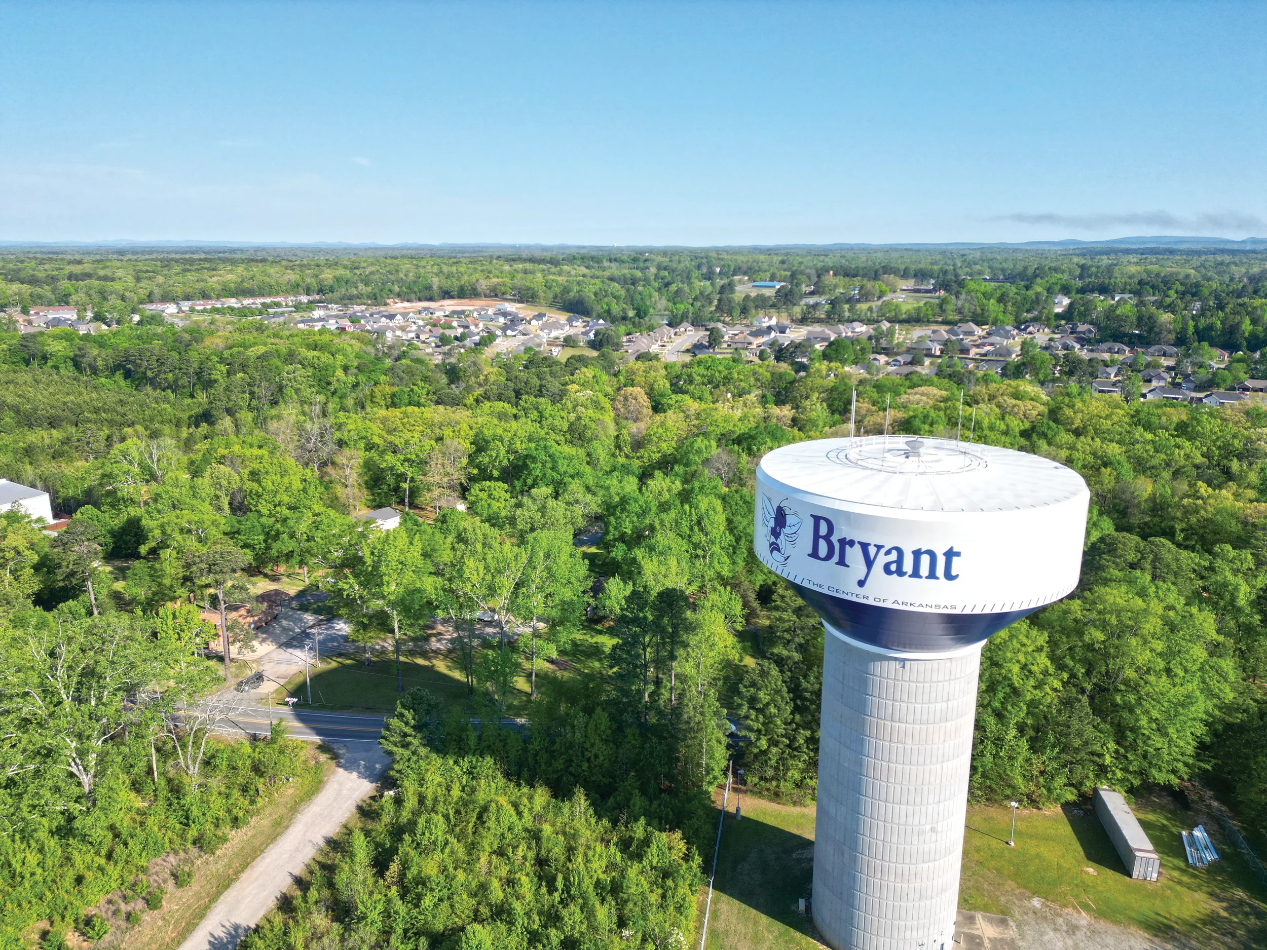 Aerial view of the Bryant, Arkansas water tower surrounded by forest, neighborhoods, and distant hills.