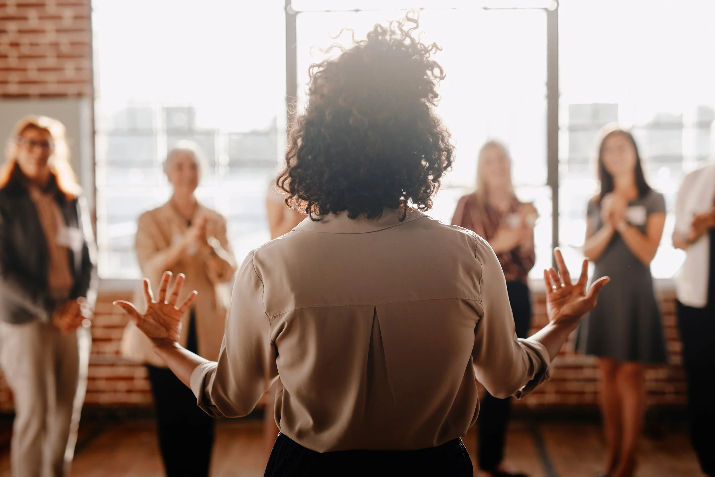 woman with her back turned speaking to a small group of other people from a platform
