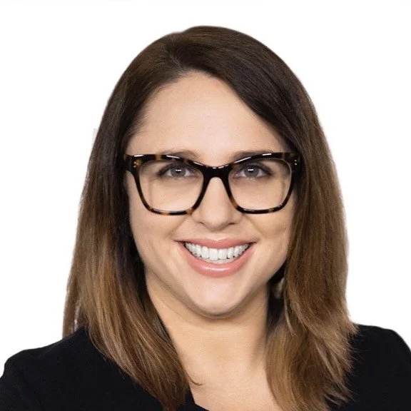 Smiling woman with straight brown hair and glasses, wearing a black top, photographed against a plain white background.