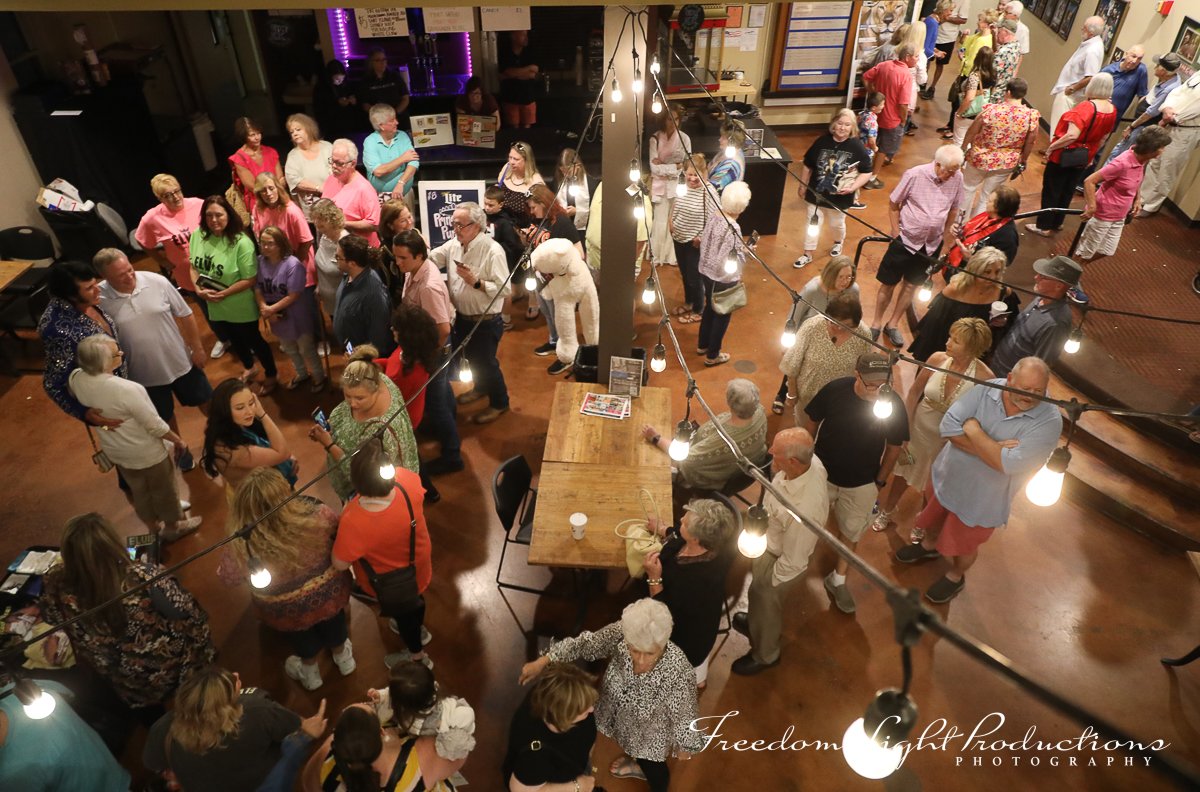 People dancing and socializing in a crowded indoor event space with string lights hanging from the ceiling.