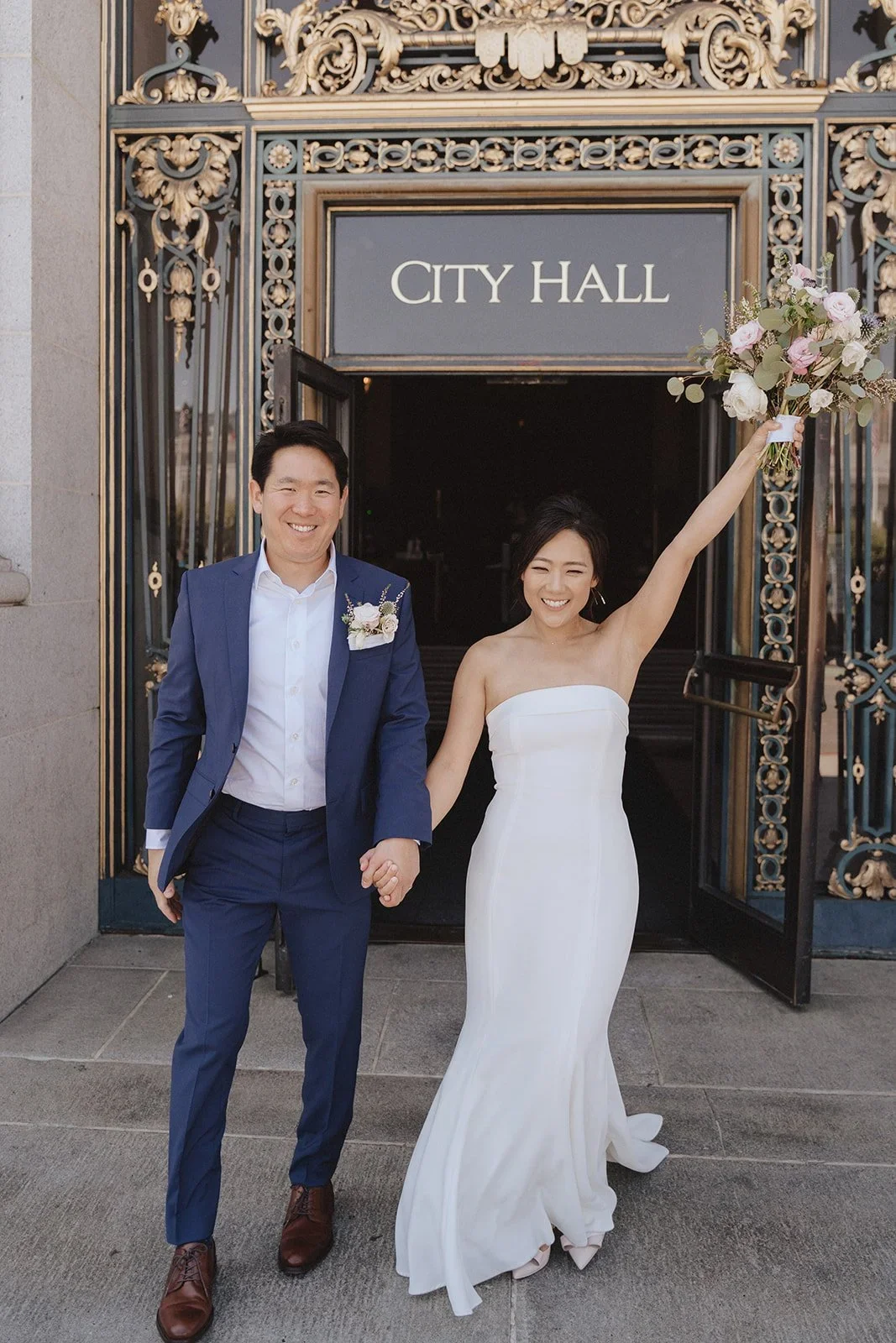 Couple walking out of downtown SF city hall cheering, taken by san francisco city hall wedding photographer​
