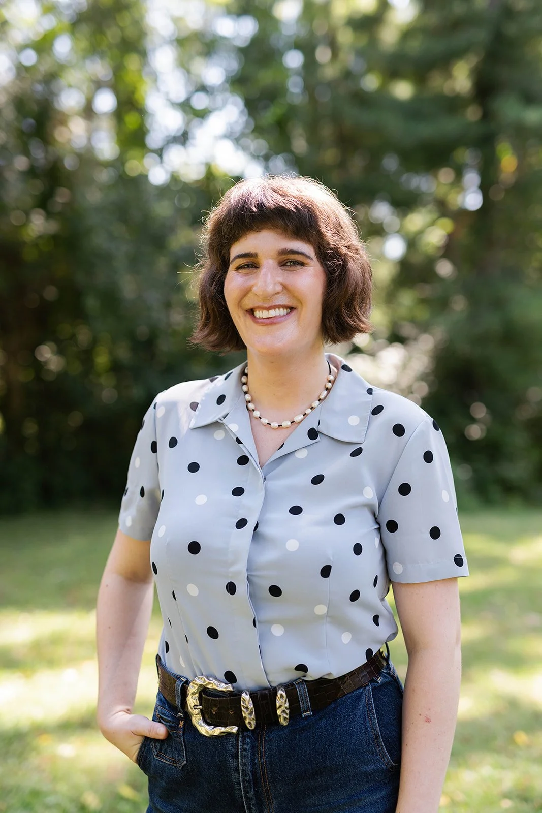 Lily Duffy, LCSW stands in an open, grassy space with green trees in the background.