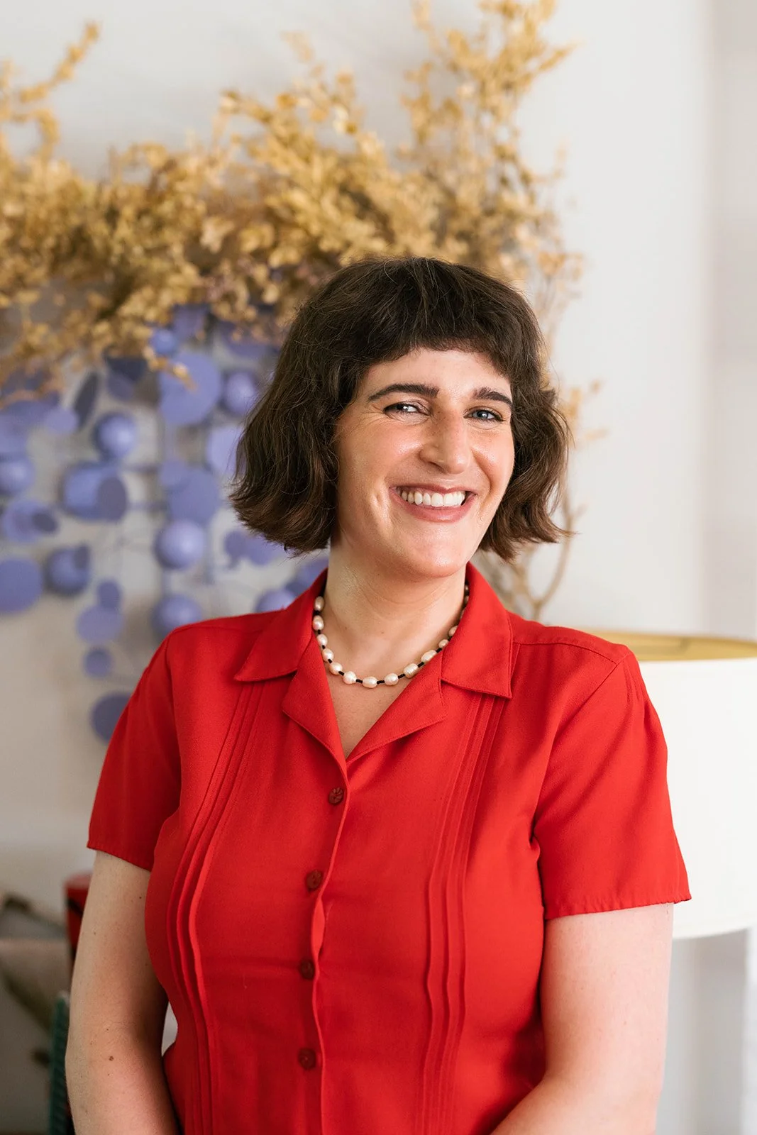 Lily Duffy, LCSW stands in front of colorful, textured wall art in their office.