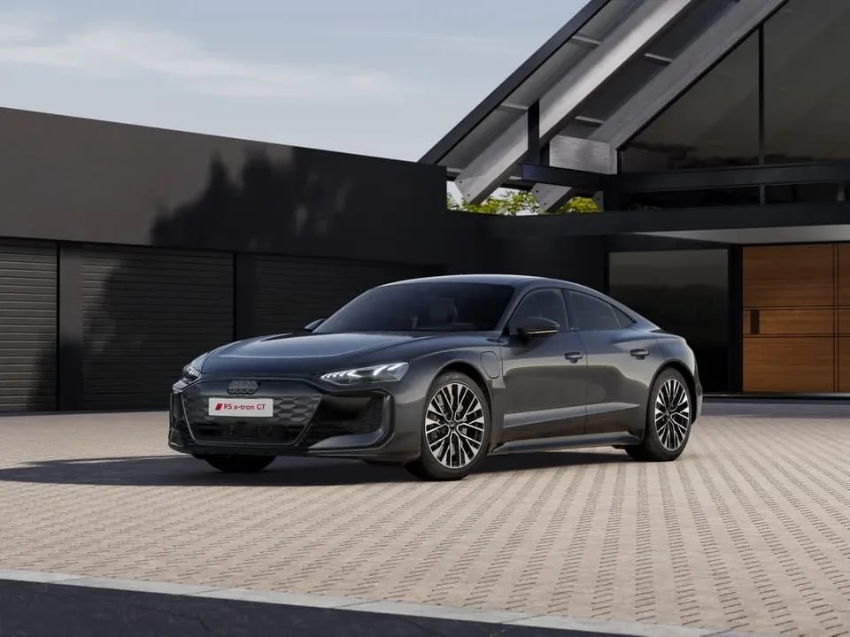 Ein schwarzer Audi RS e-tron GT elektrischer Sportwagen parkt vor modernem Haus mit dunklen Wänden und großen Fenstern.