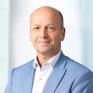 Porträt eines Mannes in einem blauen Anzug vor hellem Hintergrund.