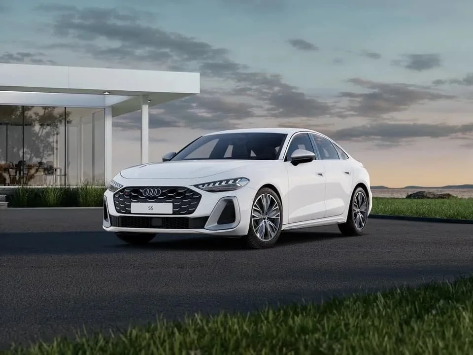 Ein weißer Audi-S51-Limousine parkt vor einem modernen Gebäude bei Sonnenuntergang, mit einem offenen Himmel im Hintergrund.