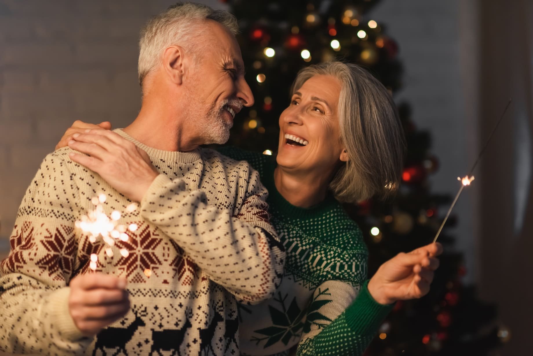 An attractive older couple laugh and smile at each other, they are wearing festive jumpers