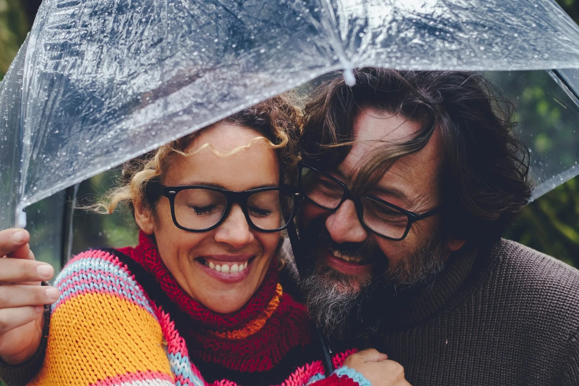An attractive couple in their forties huddle happily under an umbrella