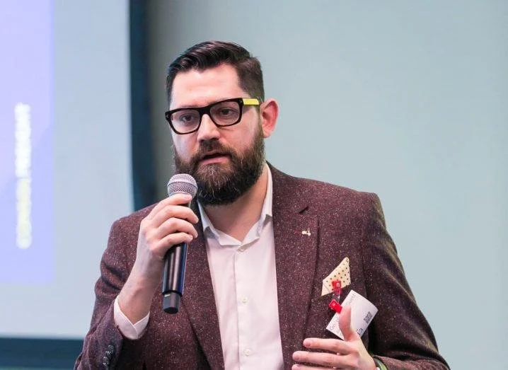 A man with glasses and a beard speaking into a microphone during a presentation.