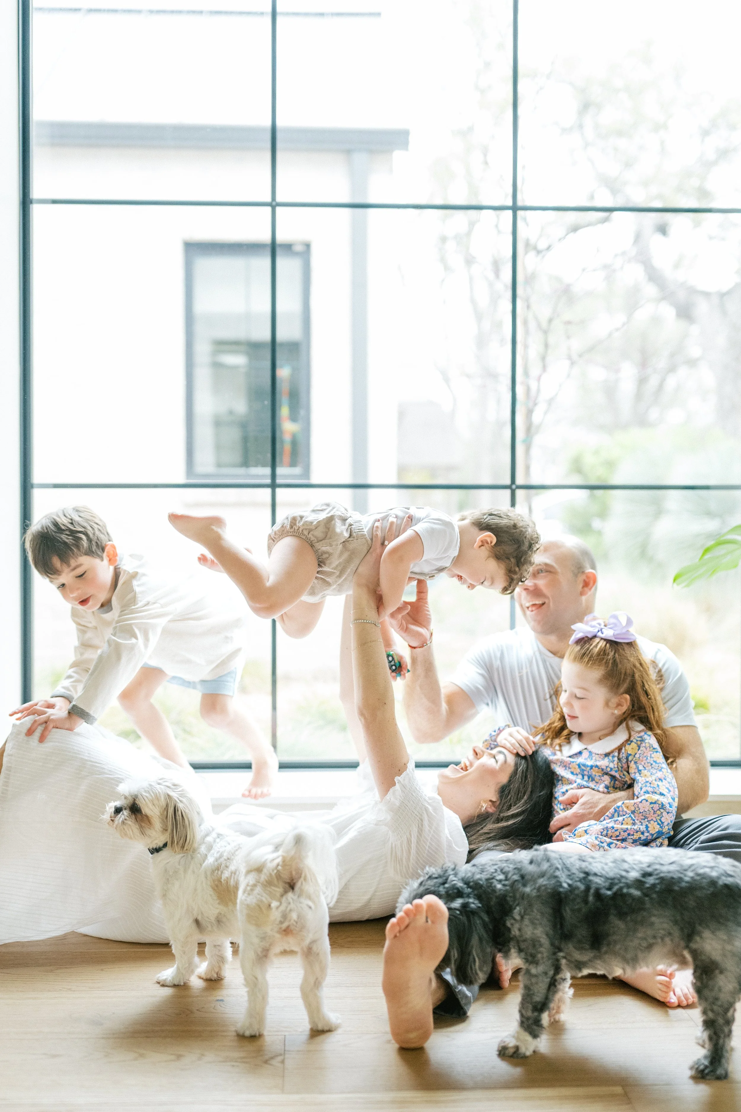 Mom laying down on her back with her head on her husband's lap while she is playing with her kids during an in-home family session in Austin, Texas.