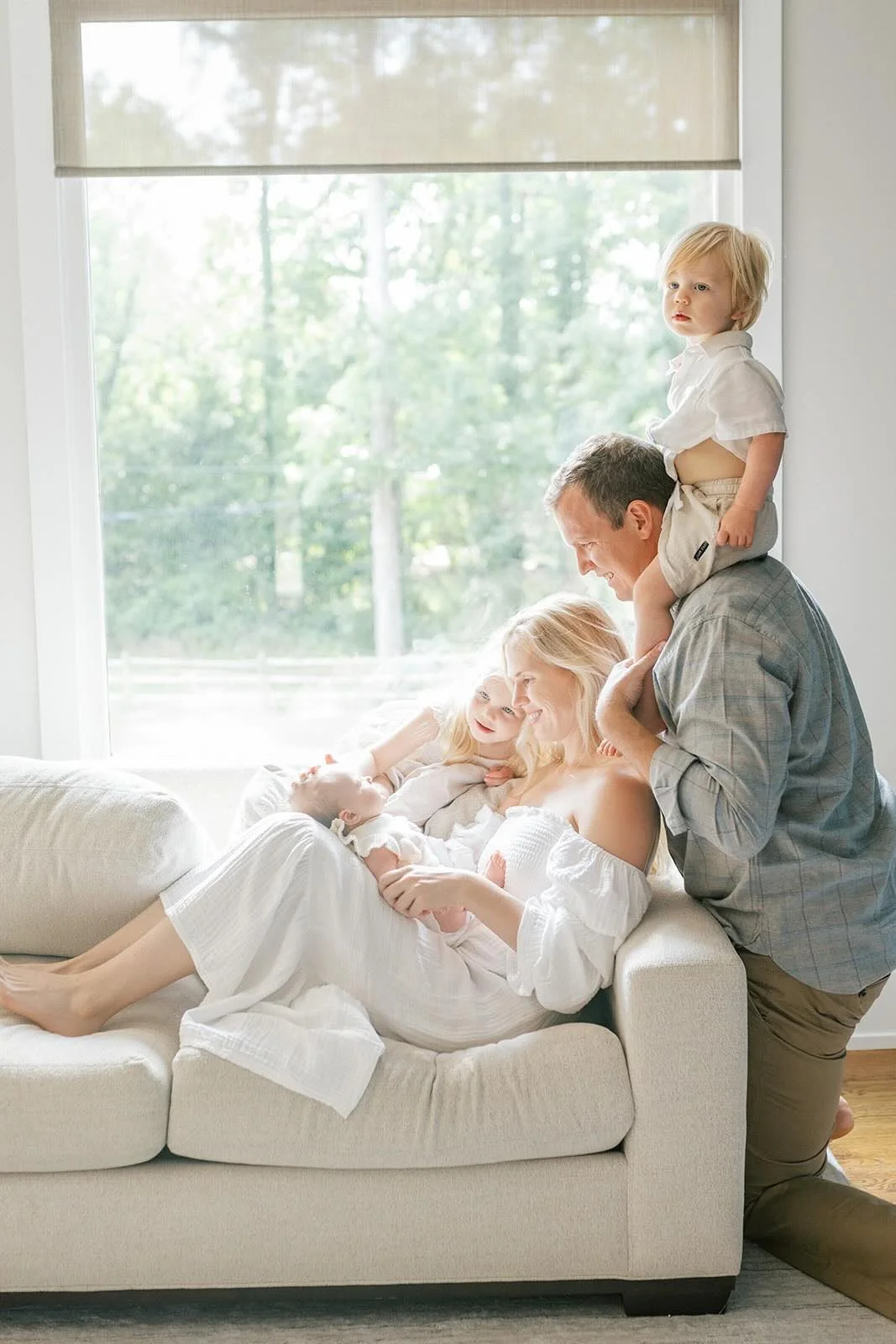 Family looking at new baby lovingly in front in the natural light from the large window - Raleigh Newborn Photographer