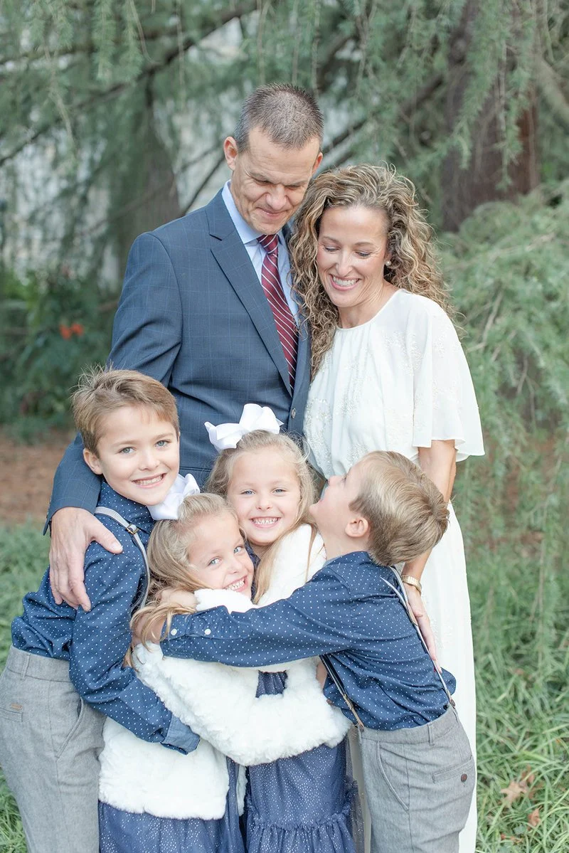 four children hugging each other and laughing with their parents behind them and smiling down at them during a beautiful spring evening by Kelly Bullock Photography.