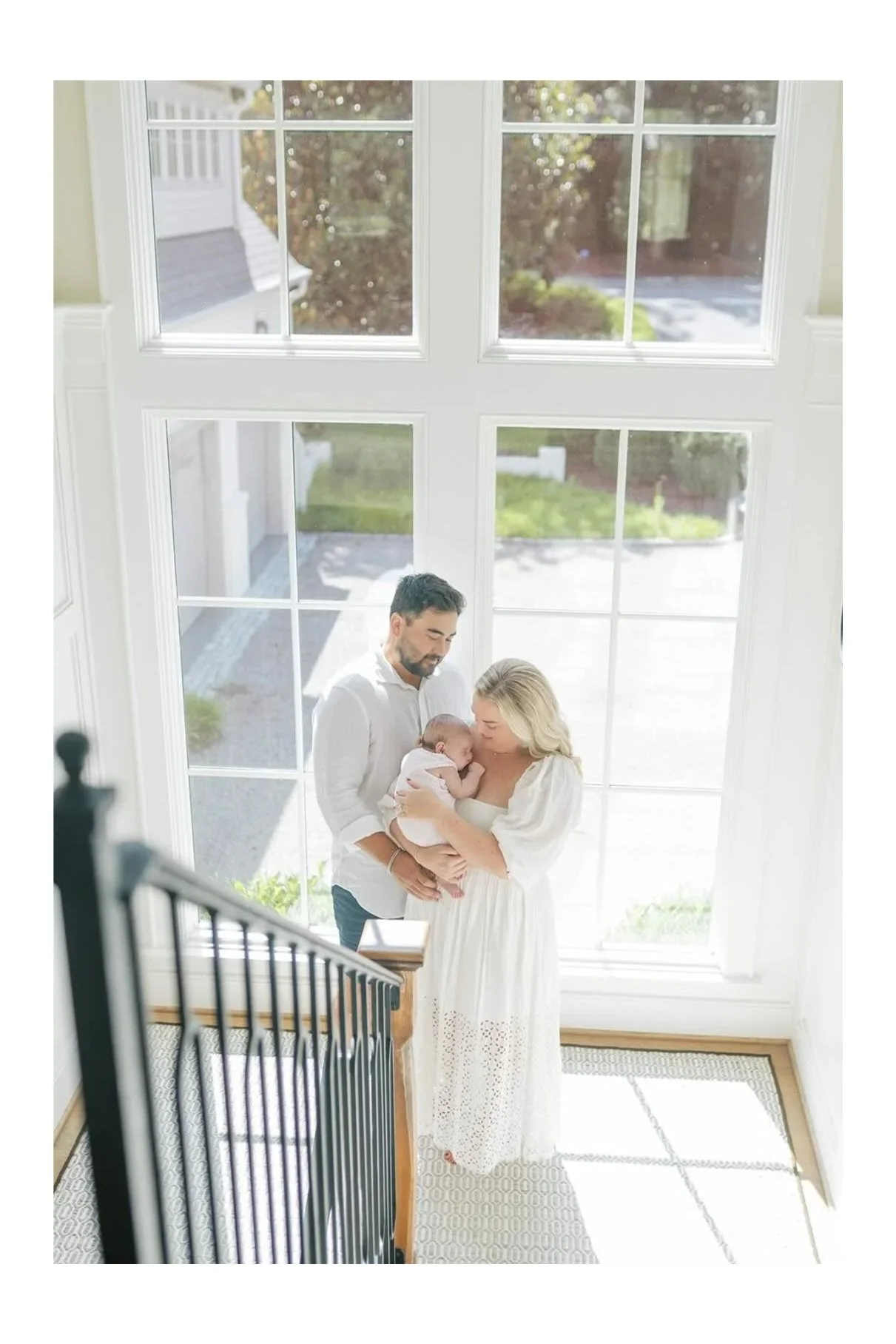 Mom and Dad holding a newborn baby in the natural light on their stairs - Raleigh Newborn Photographer