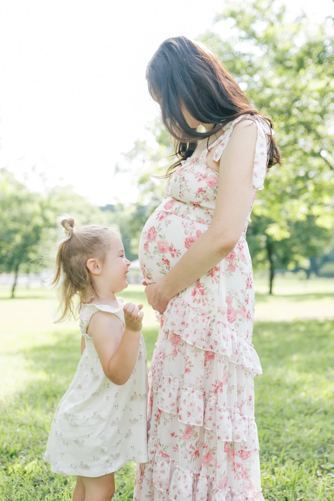 Mother holding her baby bump while toddler smiles up at her during outdoor pregnancy announcement photo ideas session in Raleigh.
