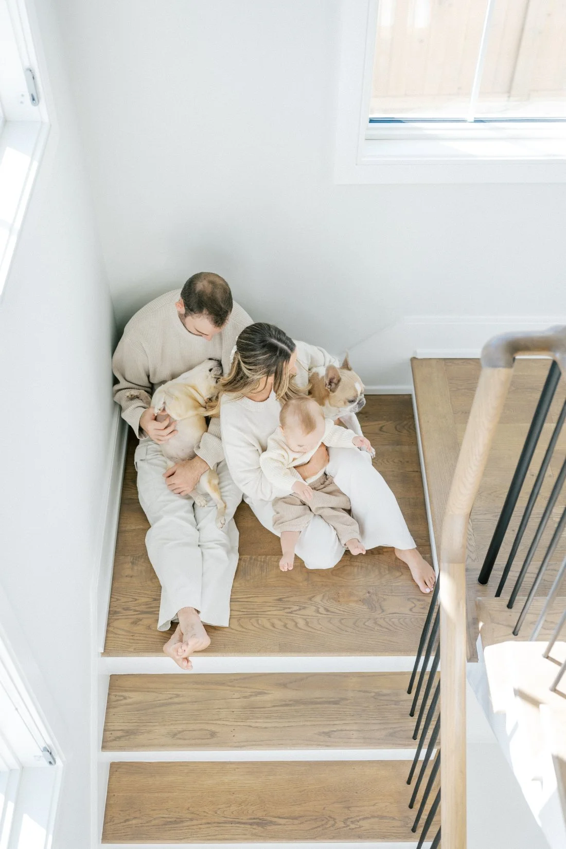 Cozy in-home family portraits with dogs showing parents sitting on stairs holding baby with their pup beside them