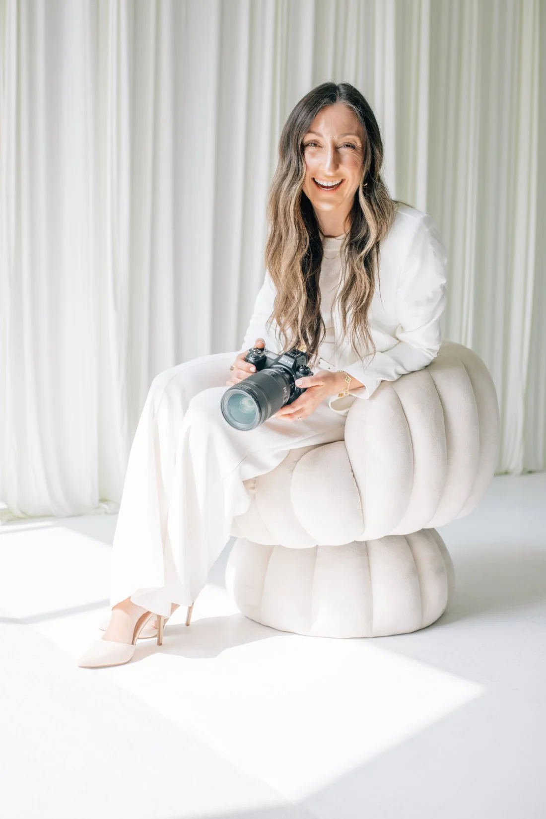 Kelly Bullock smiling with her camera in a bright studio, sharing insights on creating a thoughtful photography client experience.