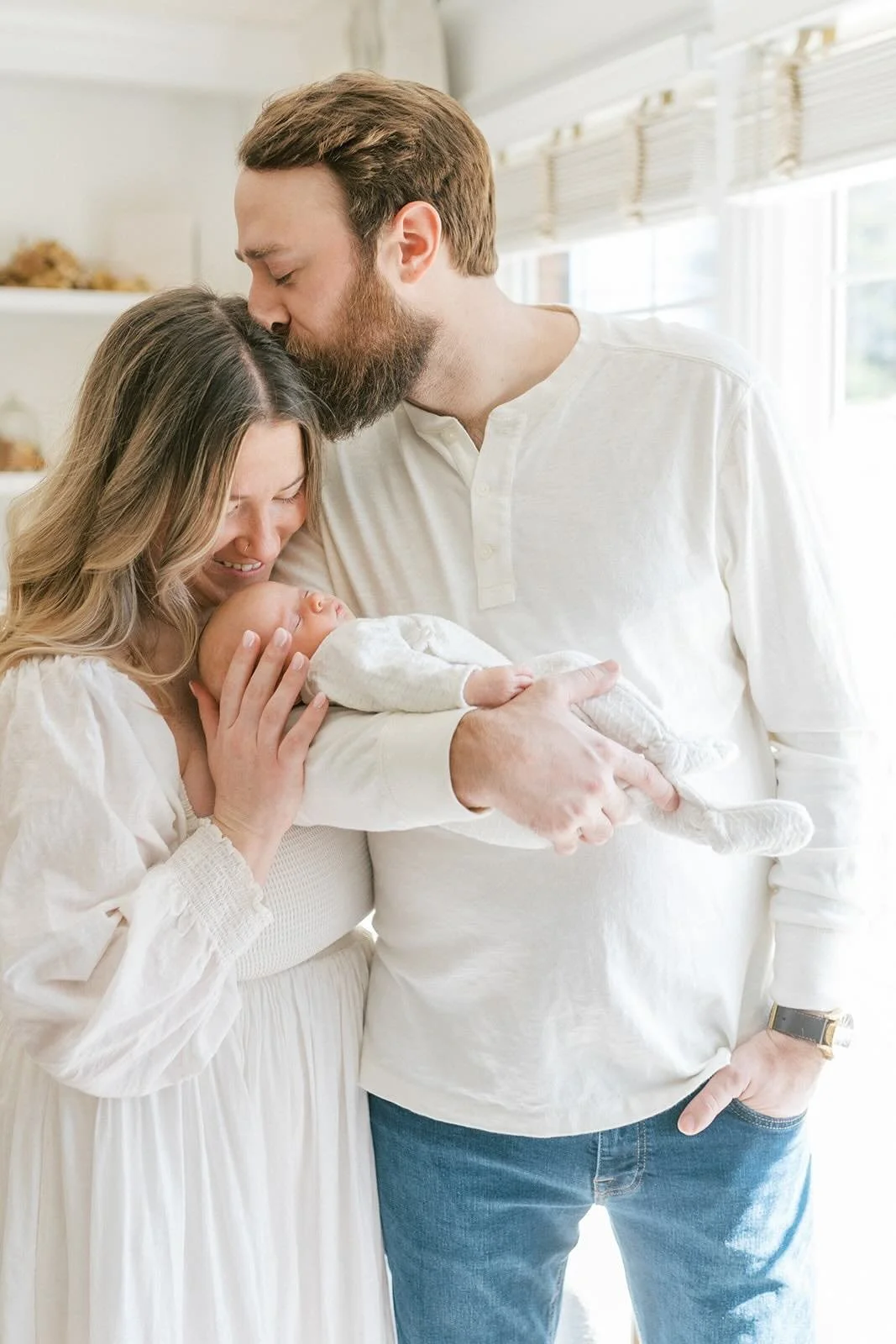 Dad holding baby while giving mom a kiss - Raleigh Newborn Photographer