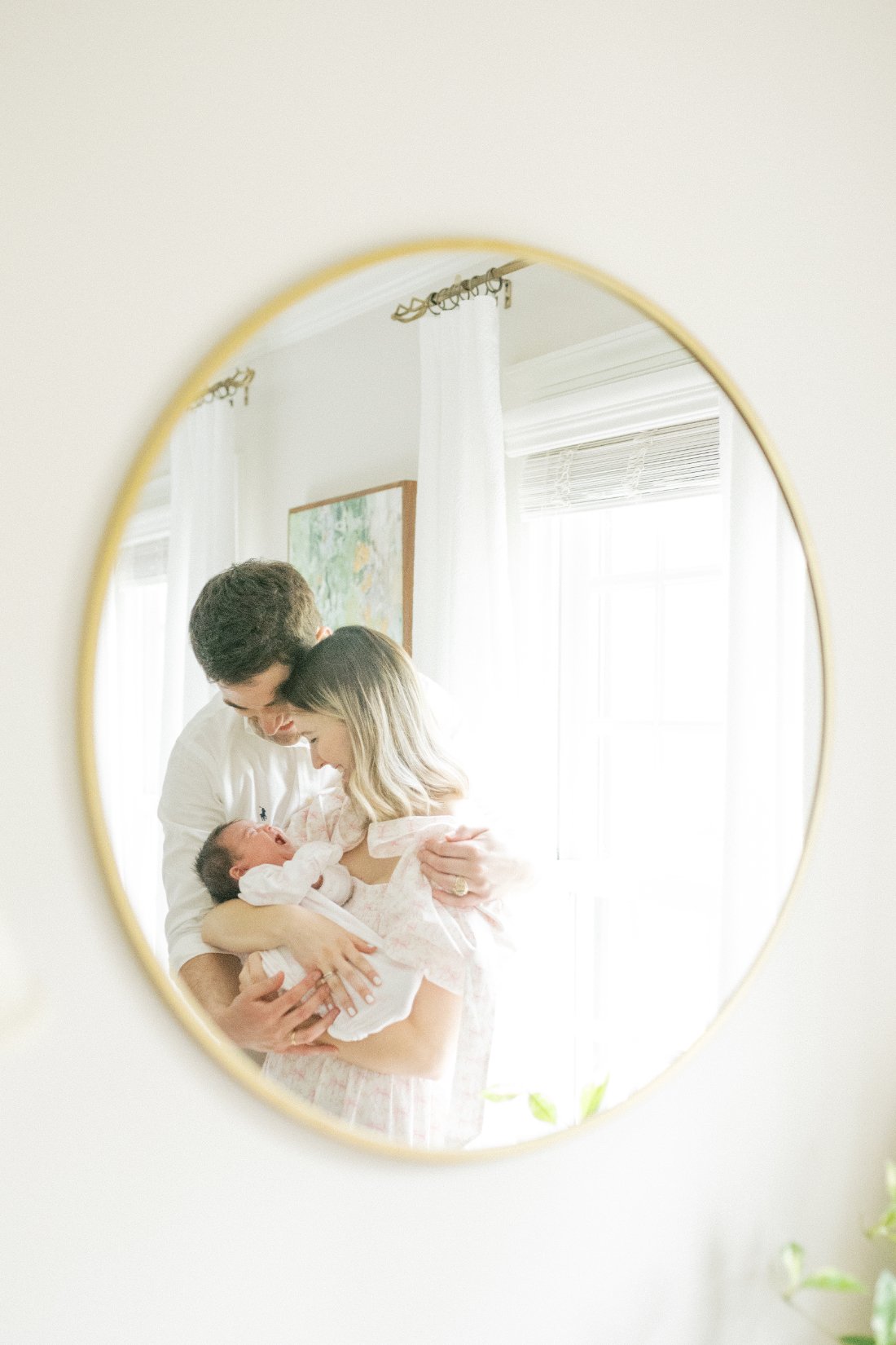 Parents cuddling their newborn baby together, reflected in a mirror during a lifestyle newborn session with a Raleigh photographer