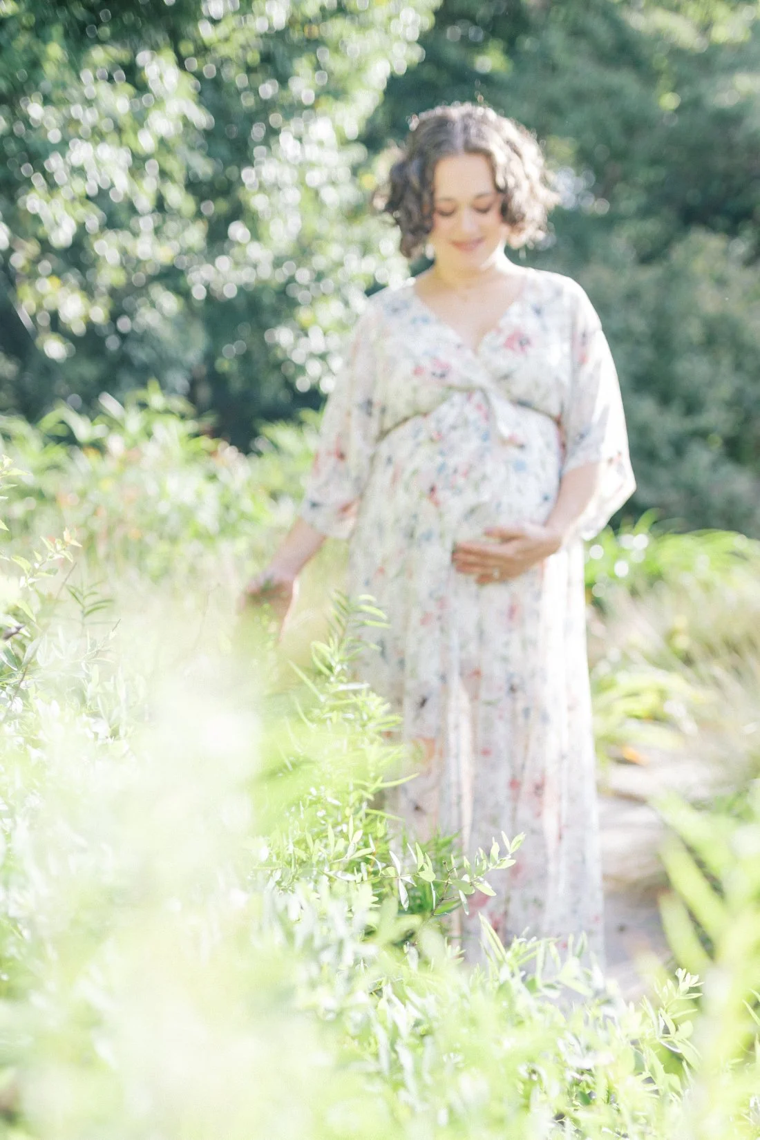Pregnant mother walking through garden greenery during soft natural light maternity session for pregnancy announcement photo ideas.