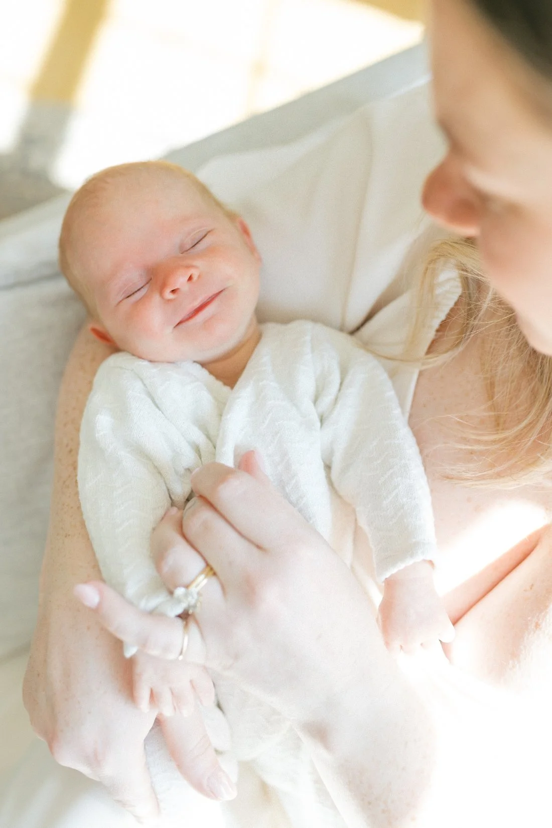 Raleigh photographer documenting a smiling newborn resting peacefully in their mother's arms during an in-home newborn session