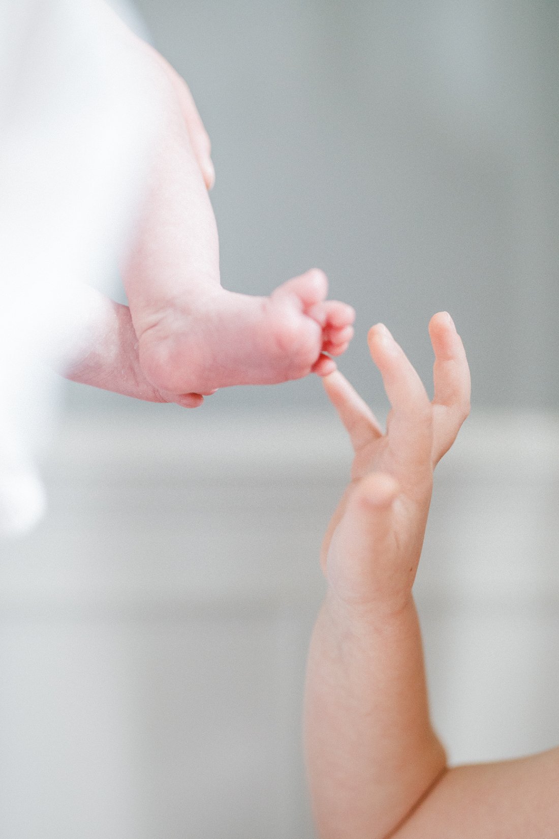 Close-up of a newborn baby’s tiny foot touching an older sibling’s hand during an at-home newborn session.