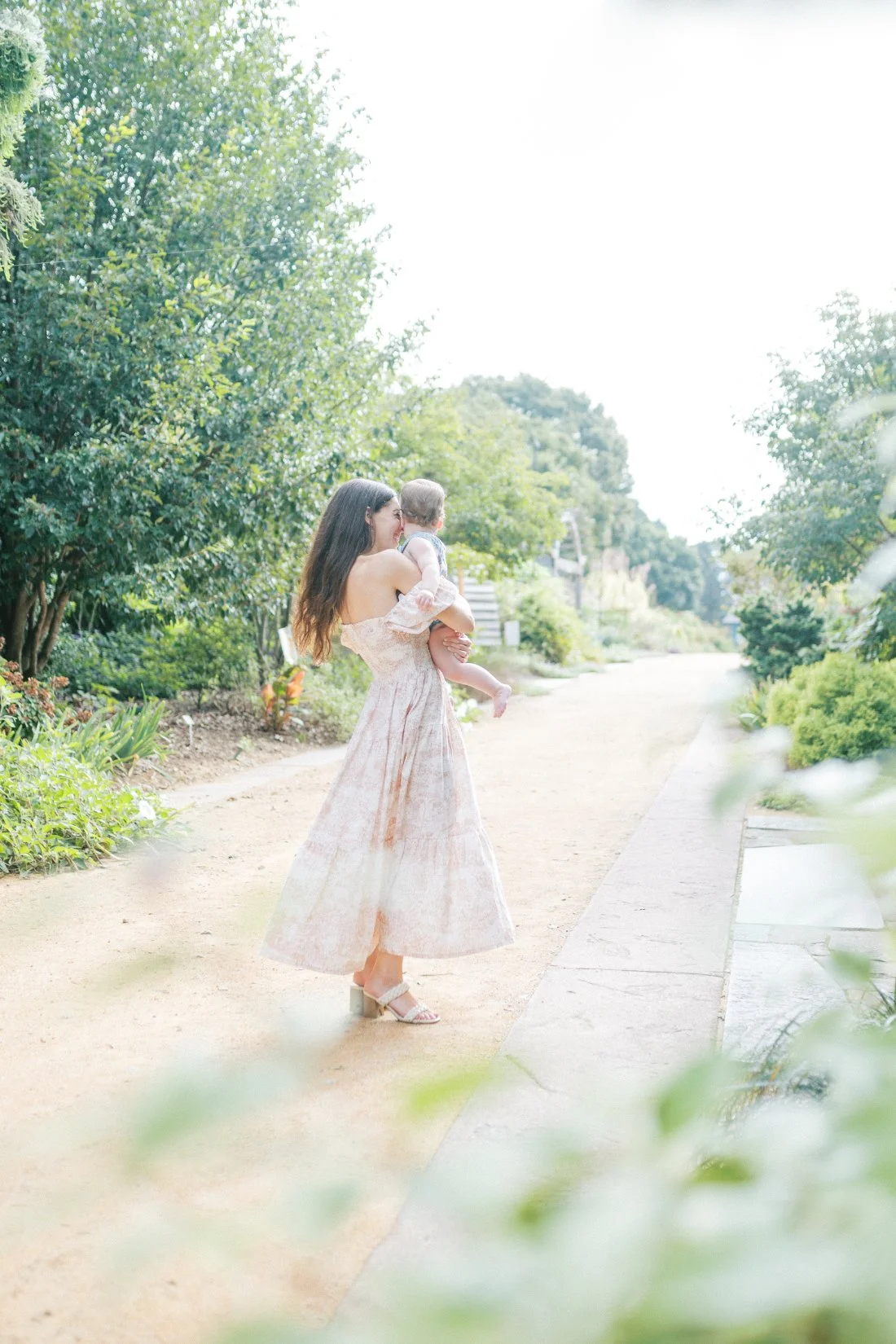 Mother walking outdoors with her baby in a flowing dress, capturing connection and movement for Mother’s Day photo gifts.