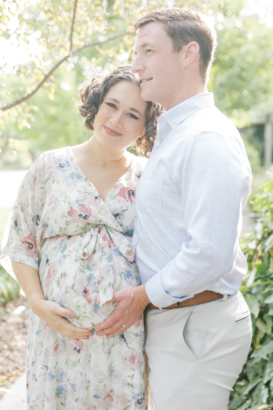 Expectant parents embracing outdoors in pastel tones during romantic early spring family photos in Raleigh.