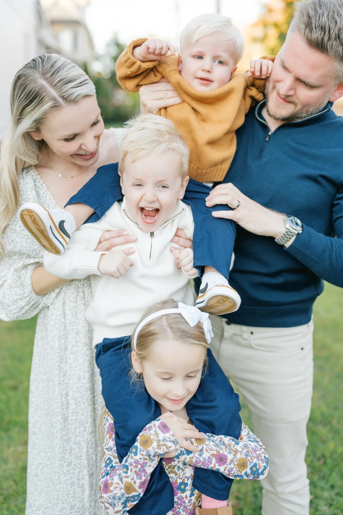 Playful fall family photos in Raleigh with three young children laughing and being held by their parents during an outdoor session.