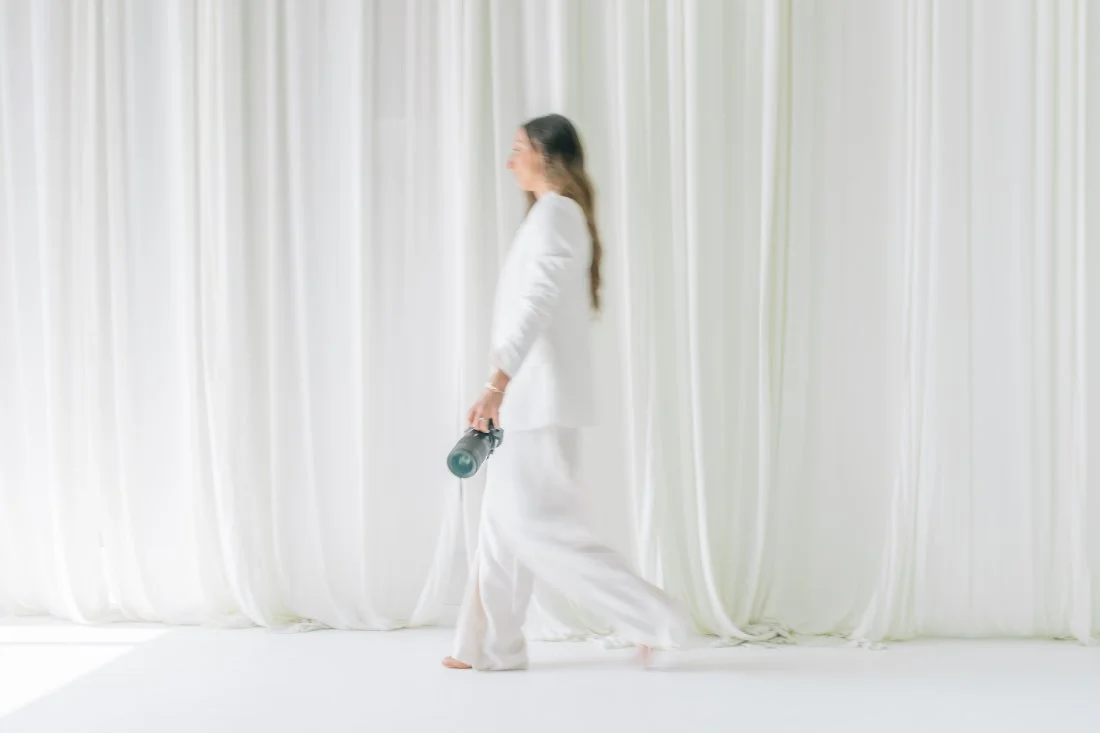 Kelly Bullock walking through a sunlit studio holding her camera, reflecting her relaxed and personal approach to family photography.