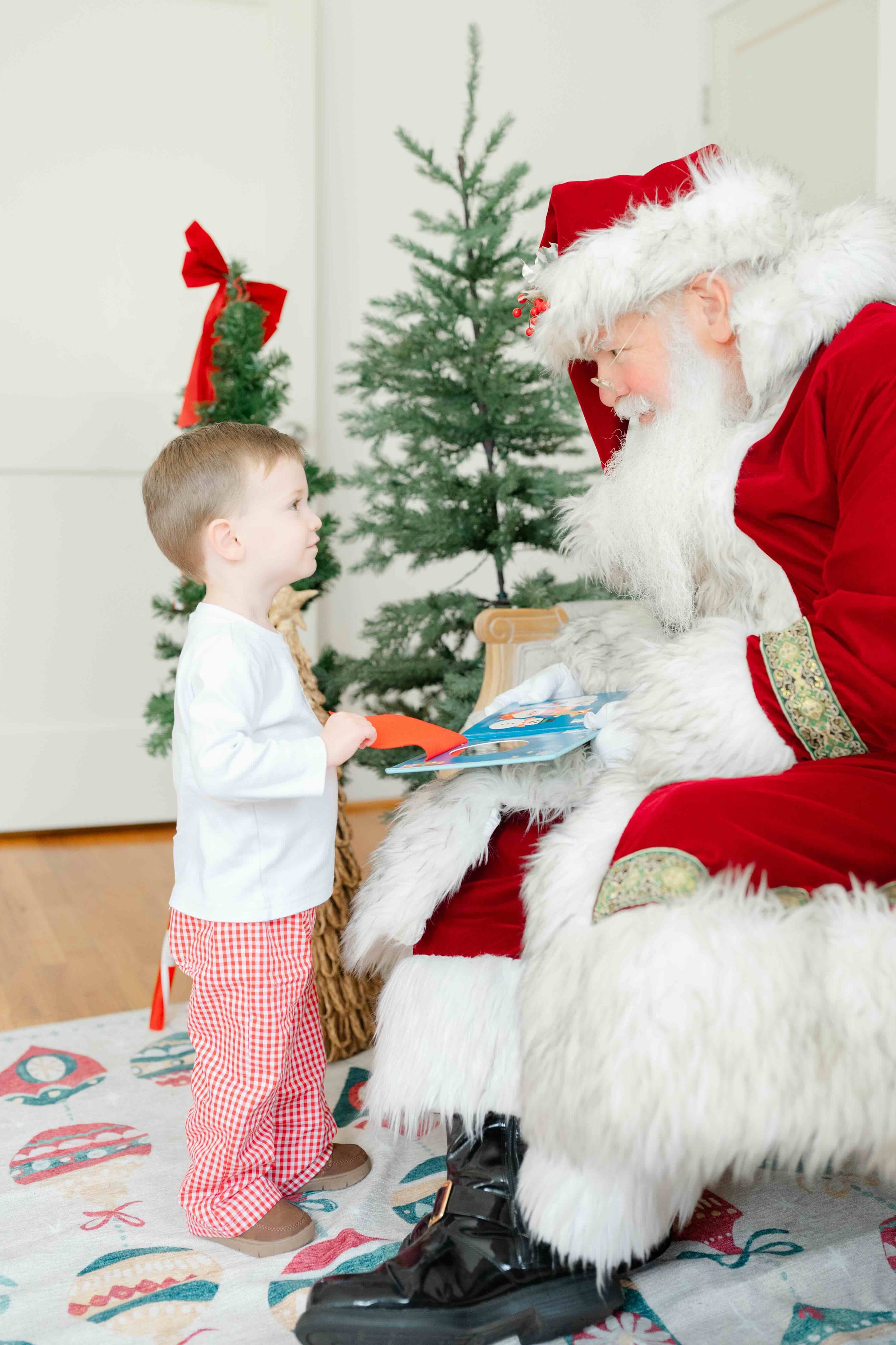 Little boy standing in front of Santa and looking at him during his photos with Santa in Raleigh wondering when he will stop believing in Santa by Kelly Bullock Photography.